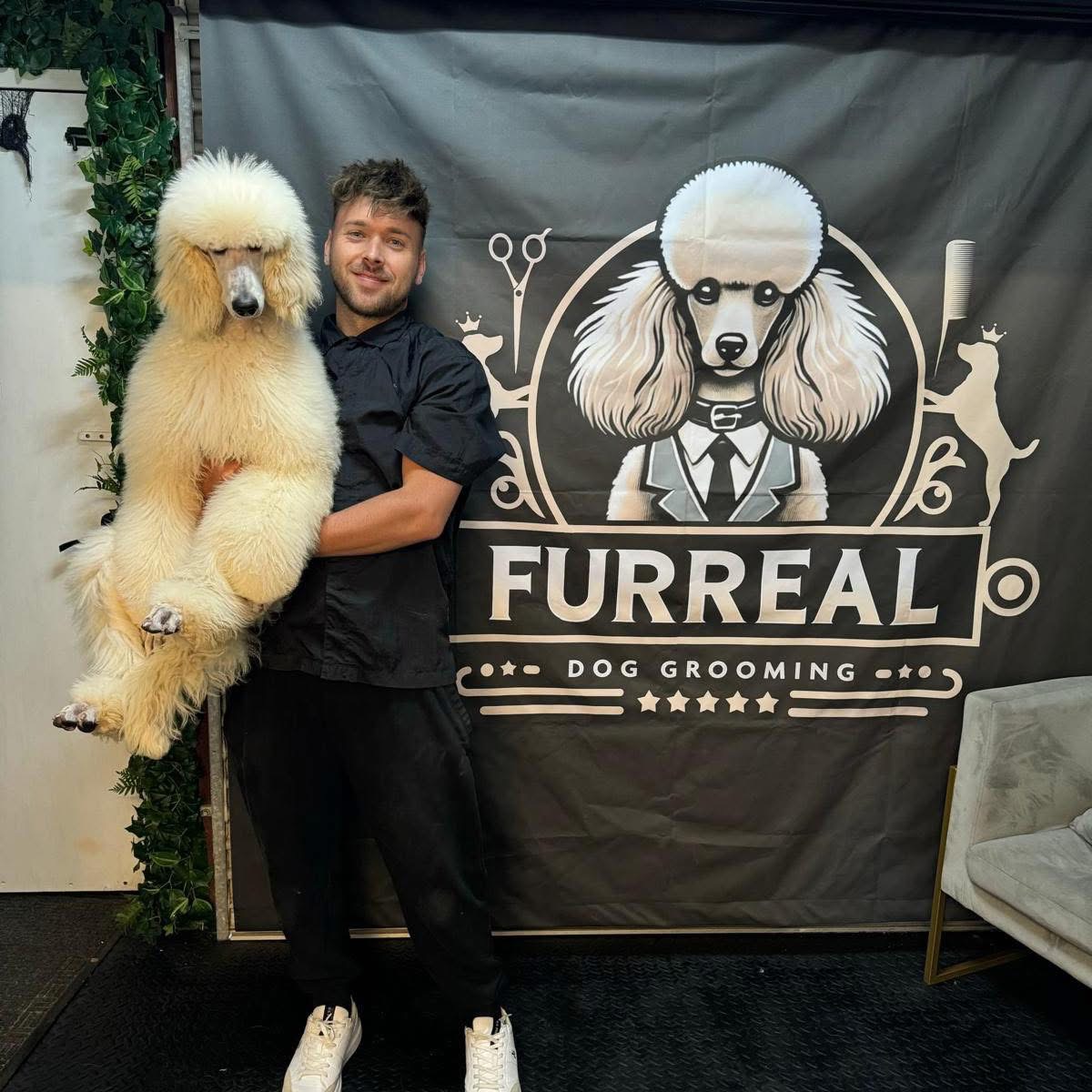 Our groomer holding a freshly groomed cream poodle in front of the FurReal Dog Grooming backdrop